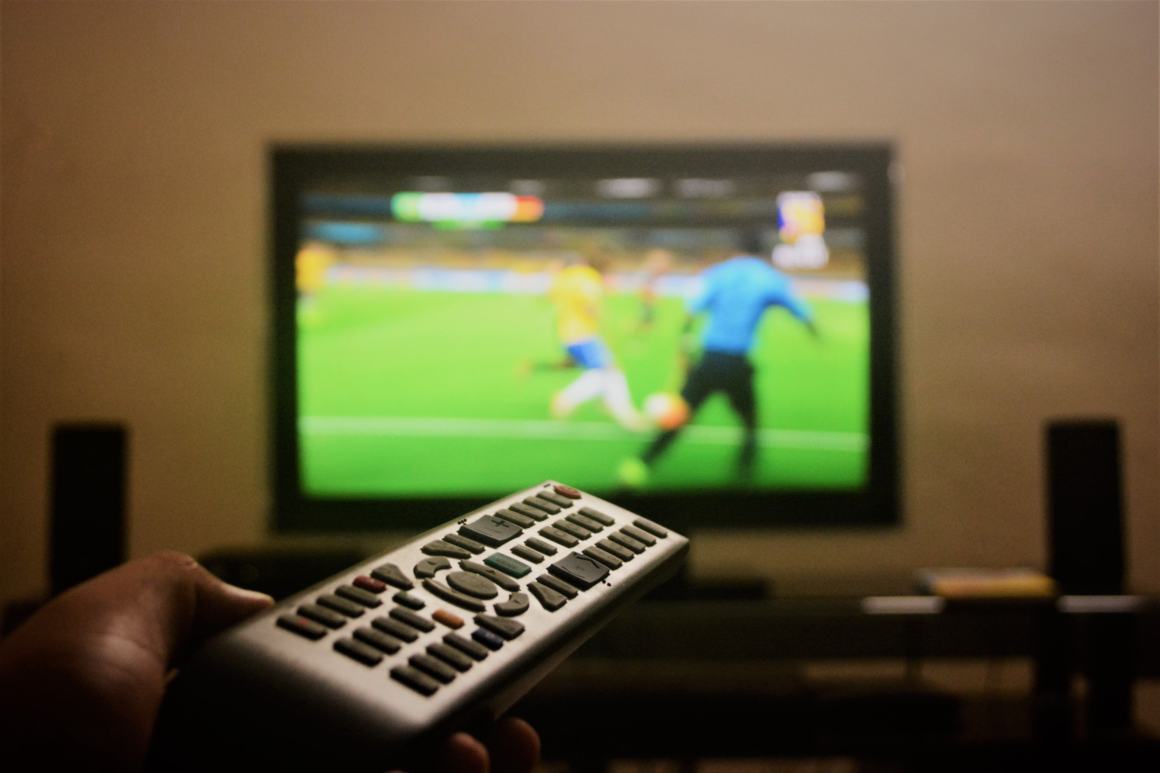 شخص يشاهد الرياضة المباشرة على تلفزيون كبير باستخدام جهاز التحكم